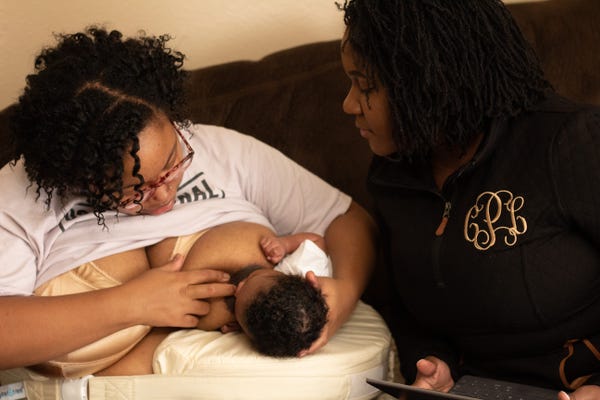 Black mother breastfeeding baby with assistance from lactation consultant 