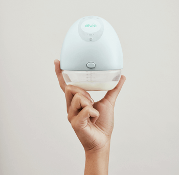 Hand holding an Elvie breast pump against a neutral background