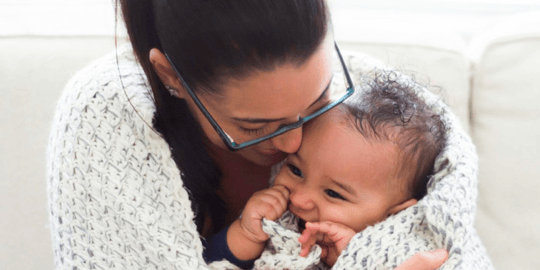 Mother cuddling her smiling baby wrapped in a knitted blanket