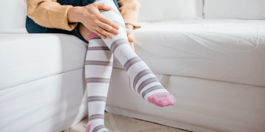 Person wearing striped compression socks while sitting on a white couch