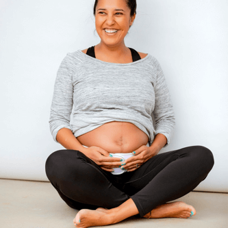 Pregnant woman sitting cross-legged and smiling while holding a lumbar support garment